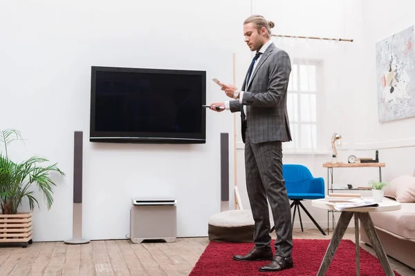 Businessman looking at smartphone and holding remote controller — Stock Photo