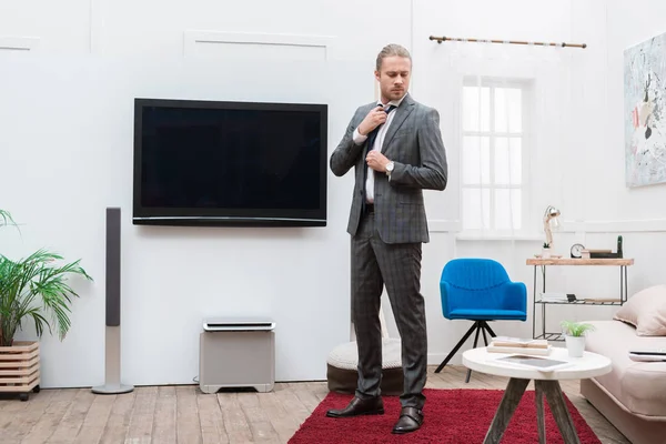 Geschäftsmann steht im Wohnzimmer und fixiert Krawatte — Stockfoto