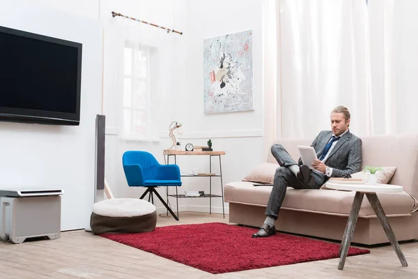 Businessman using digital tablet while sitting on sofa at home — Stock Photo