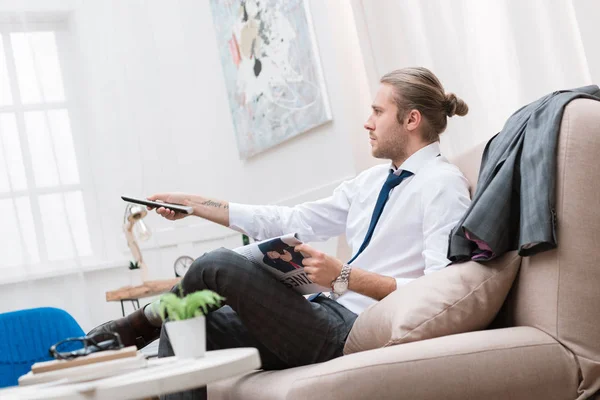 Hombre de negocios con periódico viendo la televisión en el sofá en casa - foto de stock