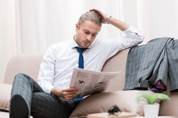 Empresário concentrado lendo jornal no sofá em casa — Fotografia de Stock
