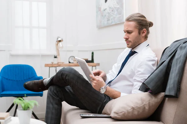 Empresário usando tablet digital enquanto sentado no sofá em casa — Fotografia de Stock