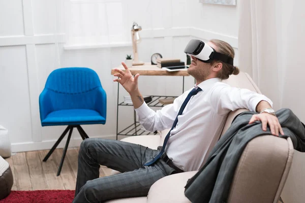 Homme d'affaires utilisant casque de réalité virtuelle assis sur le canapé à la maison — Photo de stock