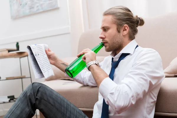 Mann sitzt auf dem Boden, trinkt Bier und liest Zeitung — Stockfoto