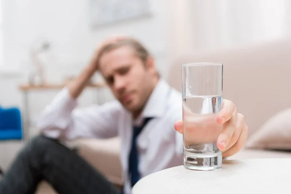 Homme d'affaires assis sur un sol à la maison et prenant un verre d'eau — Photo de stock