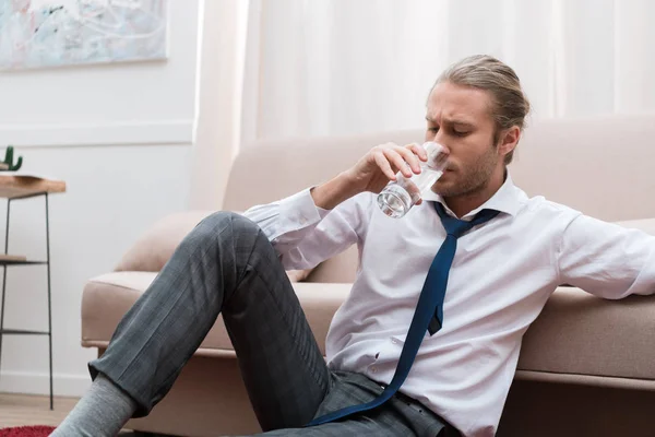 Бизнесмен сидит дома на полу и пьет воду — стоковое фото