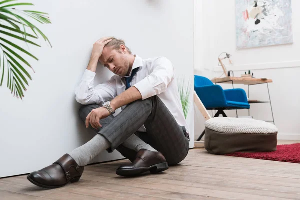 Müder Geschäftsmann sitzt zu Hause auf dem Fußboden und hat Kopfschmerzen — Stockfoto