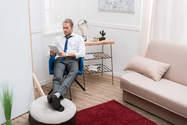 Бизнесмен сидит дома на стуле и пользуется планшетом — стоковое фото