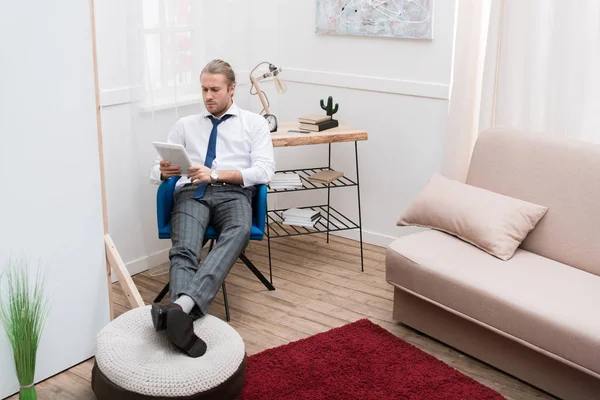 Empresario sentado en silla en casa y usando tableta - foto de stock