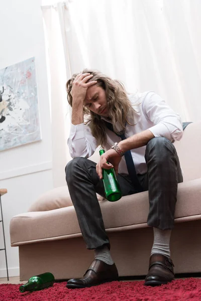 Homem sentado em um sofá com uma cerveja e com dor de cabeça — Fotografia de Stock