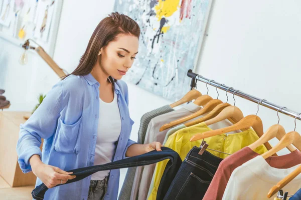 Bella designer guardando pantaloni su appendini — Foto stock