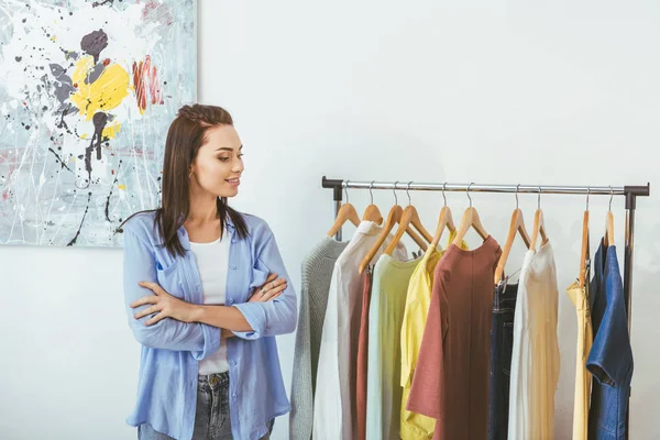 Smiling designer with crossed hands looking at clothes — Stock Photo