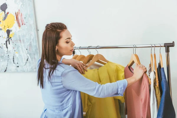 Attraente designer guardando camicie su appendini — Foto stock