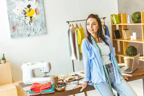 Smiling seamstress leaning on table and looking away — Stock Photo