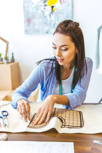 Beautiful seamstress marking pattern with piece of chalk — Stock Photo