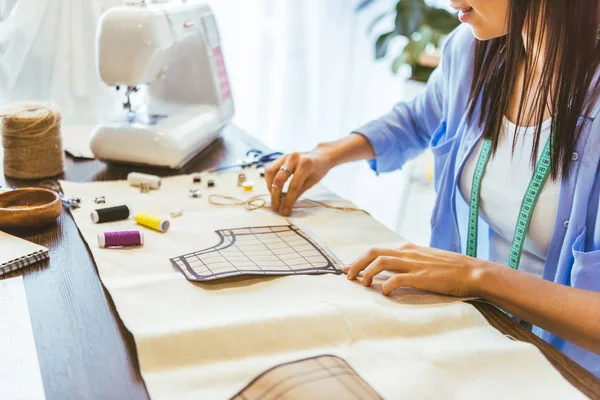 Cropped image of smiling seamstress measuring pattern at table — Stock Photo