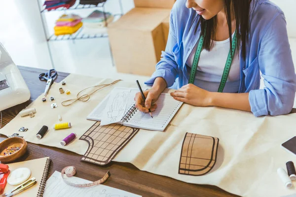 Cropped image of seamstress writing down notes to notebook — Stock Photo