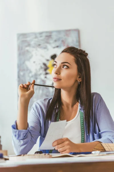 Thoughtful seamstress sitting at working table and looking up — Stock Photo