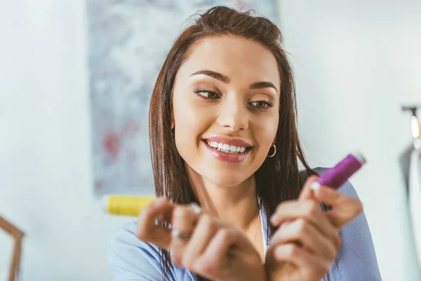 Sonriente costurera sosteniendo bobinas con hilos - foto de stock