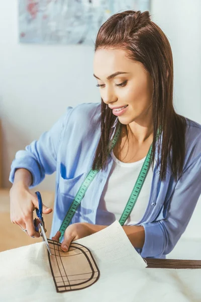 Smiling seamstress cutting fabric with scissors — Stock Photo