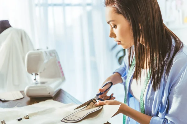 Beautiful seamstress cutting fabric with scissors — Stock Photo