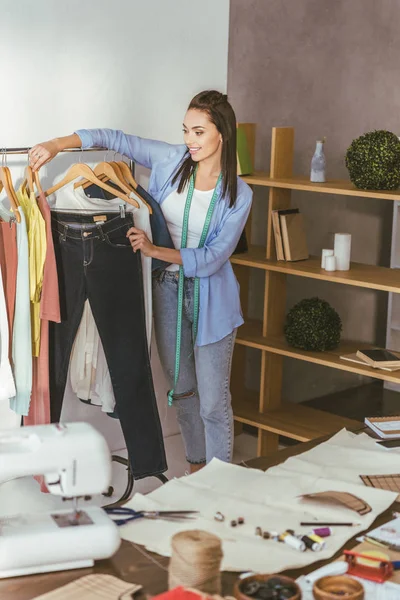 Seamstress holding trousers on hanger at her working place — Stock Photo