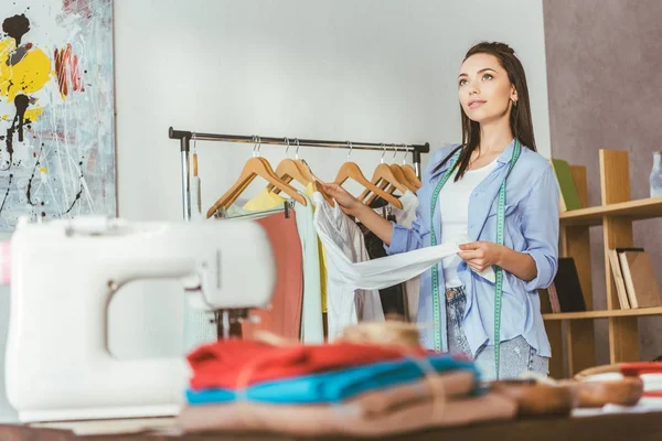 Seamstress holding shirt at hanger and looking up — Stock Photo