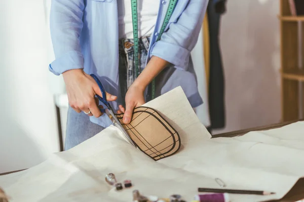 Cropped image of seamstress cutting fabric with scissors — Stock Photo