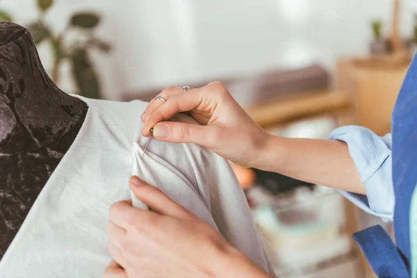 Cropped image of tailor putting pin into white dress on mannequin — Stock Photo