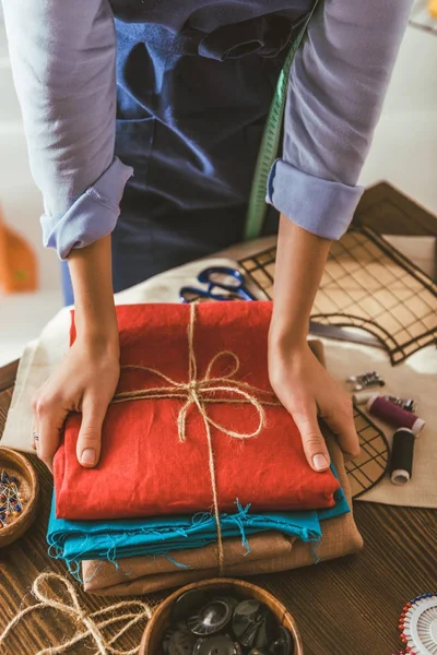 Cropped image of seamstress taking stack of colored fabric — Stock Photo