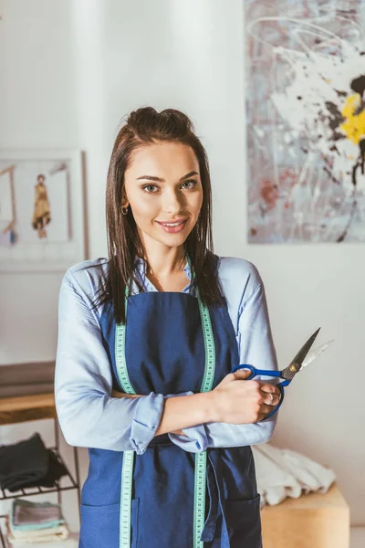 Smiling seamstress holding scissors and looking at camera — Stock Photo