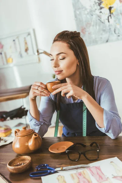 Beautiful seamstress sitting at table and drinking tea — Stock Photo