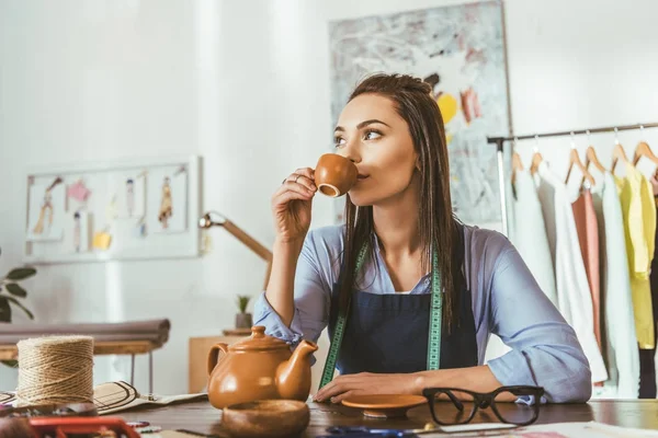 Costurera atractiva sentada en la mesa y beber té - foto de stock