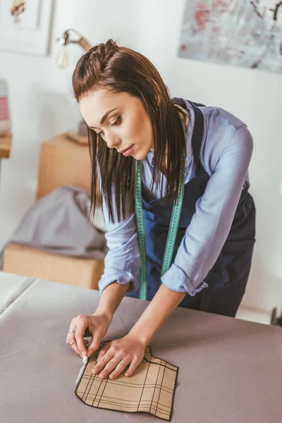 Beautiful seamstress making pattern with piece of chalk on fabric — Stock Photo