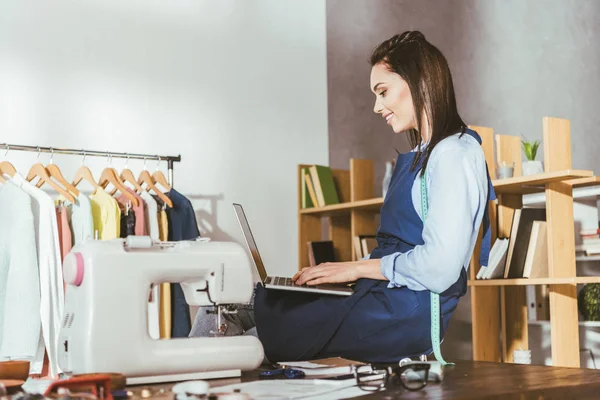 Happy seamstress sitting on table with laptop — Stock Photo
