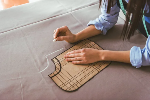 Cropped image of seamstress making pattern with piece of chalk on fabric — Stock Photo