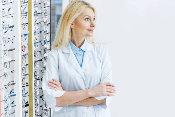 Жіночий офтальмолог стоїть в оптиці в окулярах на полицях — стокове фото