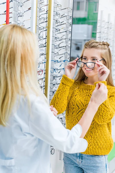 Optometrista ayudando al cliente a elegir gafas en óptica - foto de stock