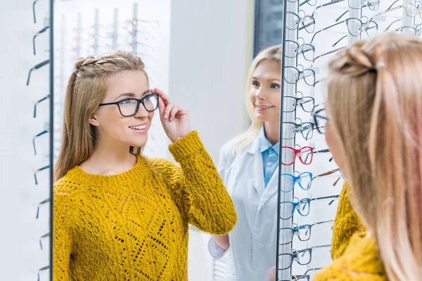Optometrista femenina ayudando al cliente a elegir gafas en óptica - foto de stock