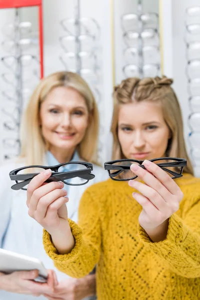 Oculista ayudando al cliente a elegir gafas en óptica - foto de stock