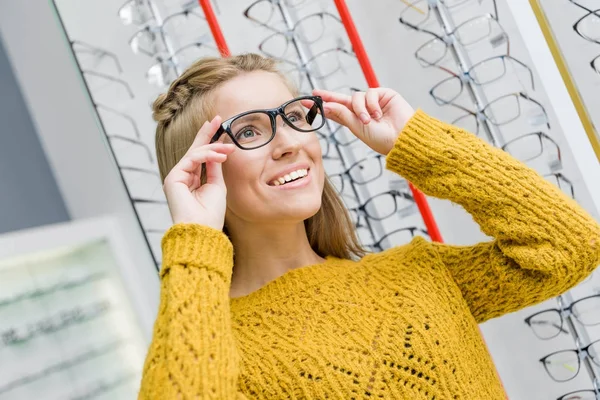 Young beautiful girl choosing eyeglasses in optics — Stock Photo
