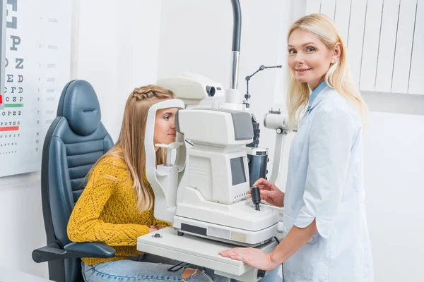 Professional female optician examining patient through slit lamp in clinic — Stock Photo