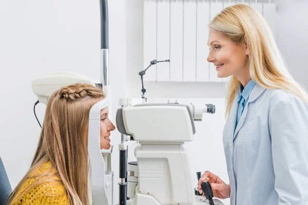 Optometrista profesional que examina a la paciente a través de lámpara de hendidura en la clínica - foto de stock