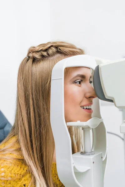 Paciente sonriente examinando sus ojos con lámpara de hendidura en la clínica — Stock Photo
