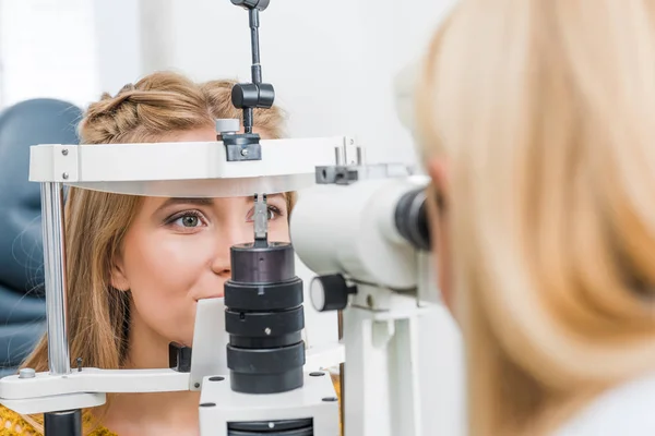 Optometrista femenina examinando paciente a través de lámpara de hendidura en clínica - foto de stock