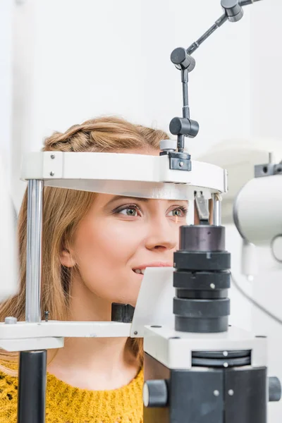 Hermosa paciente examinando sus ojos con lámpara de hendidura en la clínica - foto de stock