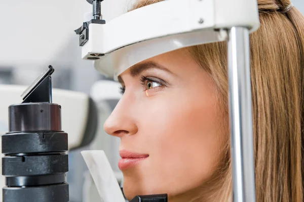 Close up de paciente atraente examinando seus olhos com lâmpada de fenda na clínica — Fotografia de Stock