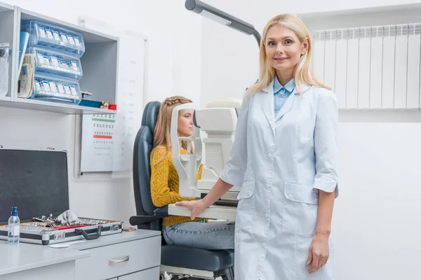 Female optometrist examining patient through slit lamp in clinic — Stock Photo