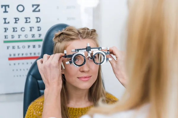 Cropped view of oculist and young patient with trial frame in clinic — Stock Photo