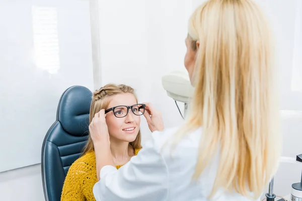 Oculista y paciente probando gafas nuevas en clínica - foto de stock